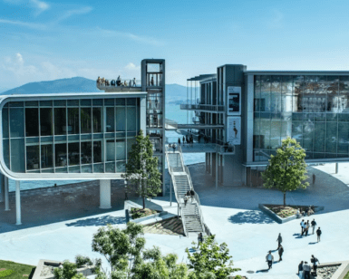 Con vistas al agua, el moderno Centro Botín cuenta con elegantes escaleras llenas de gente. Enmarcado por frondosos árboles y una majestuosa montaña bajo un cielo azul vibrante, Descubre el Centro Botín ofrece una serena fusión de naturaleza e innovación. - ForTwo - Planes para parejas