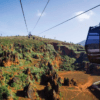 Descubra el parque de Cabárceno en un teleférico que se desliza sobre su extensión rocosa y exuberante, con colinas distantes que se despliegan bajo un cielo azul claro. - ForTwo - Planes para parejas
