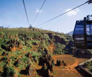 Descubra el parque de Cabárceno en un teleférico que se desliza sobre su extensión rocosa y exuberante, con colinas distantes que se despliegan bajo un cielo azul claro. - ForTwo - Planes para parejas