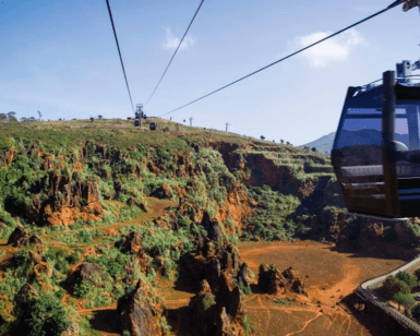 Descubra el parque de Cabárceno en un teleférico que se desliza sobre su extensión rocosa y exuberante, con colinas distantes que se despliegan bajo un cielo azul claro. - ForTwo - Planes para parejas