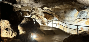 Explora el sendero iluminado de Descubre la Cova de S’Aigua en Menorca, con impresionantes formaciones rocosas y una resistente barandilla de metal para mayor seguridad. - ForTwo - Planes para parejas