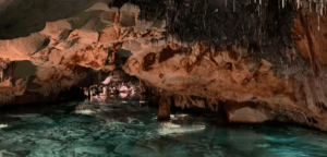 Explora "Descubre la Cova de S’Aigua en Menorca", donde delicadas estalactitas cuelgan sobre una piscina turquesa, reflejando bellamente las fascinantes formaciones rocosas. - ForTwo - Planes para parejas