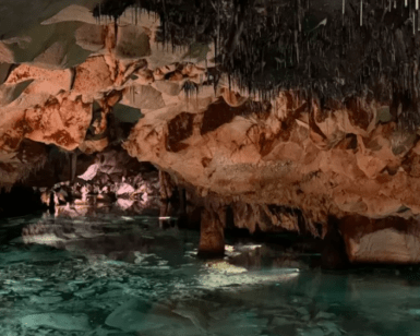 Explora "Descubre la Cova de S’Aigua en Menorca", donde delicadas estalactitas cuelgan sobre una piscina turquesa, reflejando bellamente las fascinantes formaciones rocosas. - ForTwo - Planes para parejas