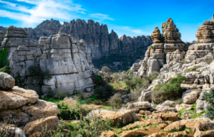 Experimente "Descubre la Historia y Naturaleza de Antequera", donde paisajes rocosos con formaciones altas y estratificadas se fusionan con una exuberante vegetación bajo un cielo azul brillante, combinando naturaleza e historia sin esfuerzo. - ForTwo - Planes para parejas