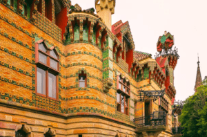 La Entrada al Capricho de Gaudí presenta una fachada colorida y ornamentada con intrincados patrones de ladrillos y azulejos, elegantes arcos y encantadores balcones, que recuerdan el estilo caprichoso de Gaudí. - ForTwo - Planes para parejas