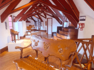 La sala refleja los intrincados diseños de la Entrada al Capricho de Gaudí, con muebles de madera, bancos tallados y vigas de madera roja en el techo. - ForTwo - Planes para parejas