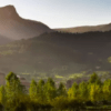 La tranquila escena del pueblo bajo un cielo soleado y despejado con montañas, árboles y una iglesia notable evoca la tranquilidad de una "Escapada al Salto del Nervión". - ForTwo - Planes para parejas