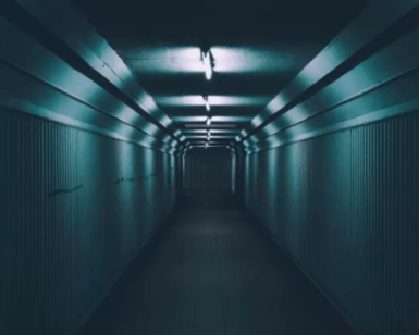 El túnel angosto y poco iluminado de Mérida, con paredes corrugadas y luces fluorescentes en el techo, recuerda a una escena de Escape Room en Mérida, mientras se aleja siniestramente hacia la oscuridad. - ForTwo - Planes para parejas