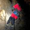 Vestida con un equipo rojo, una persona encarna el espíritu de "Espeleología en la Sierra de las Nieves", haciendo rappel con gracia dentro de una cueva rocosa. - ForTwo - Planes para parejas