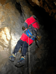 Vestida con un equipo rojo, una persona encarna el espíritu de "Espeleología en la Sierra de las Nieves", haciendo rappel con gracia dentro de una cueva rocosa. - ForTwo - Planes para parejas