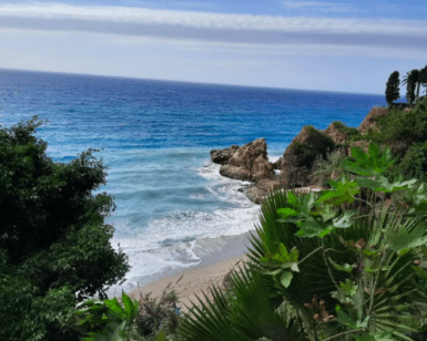 Disfrute de una vista impresionante de la costa rocosa cerca de Frigiliana durante la "Excursión a Nerja, Frigiliana y El Acebuchal", donde la exuberante vegetación domina el océano bajo un cielo parcialmente nublado. - ForTwo - Planes para parejas