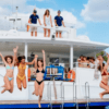 En un día soleado, un grupo de personas salta alegremente de un barco a aguas cristalinas durante su Excursión en Barco en el sur de Menorca. - ForTwo - Planes para parejas