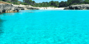 Las aguas turquesas, las costas rocosas y los frondosos árboles bajo un cielo despejado en el sur de Menorca crean un telón de fondo ideal para la Excursión en Barco en el sur de Menorca. - ForTwo - Planes para parejas