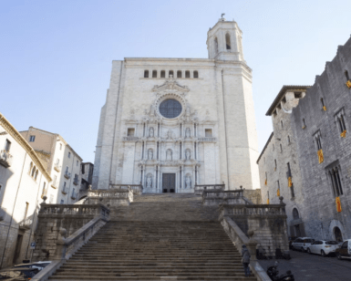 Una amplia escalera de piedra conduce a un imponente edificio histórico blanco con detalles ornamentales y una ventana redonda. Explora el encanto de Girona y su impresionante arquitectura con nuestra aventura "Explora Girona en 48 Horas". - ForTwo - Planes para parejas