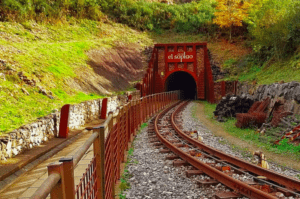 Las vías del tren conducen al encantador túnel de la mina Explora la Cueva del Soplao, rodeado de exuberante vegetación y muros de piedra, que invitan a los visitantes a explorar esta joya escondida del turismo. - ForTwo - Planes para parejas