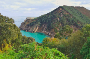 Disfrute de la vista panorámica de una exuberante costa verde, una bahía turquesa y una ladera arbolada bajo un cielo nublado en una excursión a Explora la Cueva del Soplao. Ideal para quienes buscan lo último en turismo. - ForTwo - Planes para parejas