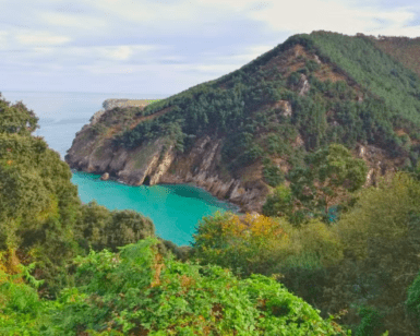 Disfrute de la vista panorámica de una exuberante costa verde, una bahía turquesa y una ladera arbolada bajo un cielo nublado en una excursión a Explora la Cueva del Soplao. Ideal para quienes buscan lo último en turismo. - ForTwo - Planes para parejas
