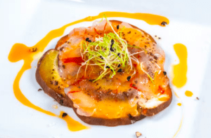 Un plato gourmet con mariscos cortados en finas lonchas, Finca de setas en Menorca, brotes frescos y una salsa vibrante presentada elegantemente en un plato blanco. - ForTwo - Planes para parejas