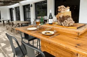 Un patio al aire libre cuenta con una mesa de madera para dos, con bebidas, platos de comida y una canasta de las mejores Finca de Setas en Menorca de Menorca como decoración. - ForTwo - Planes para parejas