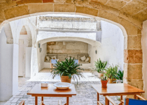 Escondido en el Corazón de Ciutadella, este acogedor patio de piedra con arcos, mesas, sillas y plantas vibrantes bajo un nicho sombreado es un refugio tranquilo que se hace eco del encanto del Hotel Nou Sant Antoni: En el Corazón de Ciutadella. - ForTwo - Planes para parejas