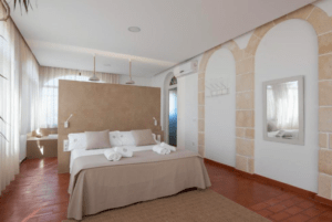 Un dormitorio sereno y minimalista que recuerda al Hotel Rural en Menorca cuenta con una cama grande, tonos neutros, un suelo de baldosas rojas, una puerta arqueada y una iluminación suave. - ForTwo - Planes para parejas