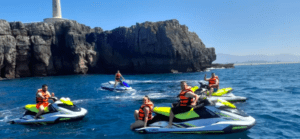 Gente disfrutando del Jet Ski por la Costa de Cantabria cerca de acantilados rocosos y un faro, con chalecos salvavidas en un día soleado. - ForTwo - Planes para parejas