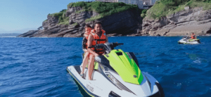 Dos amantes de las emociones fuertes con chalecos salvavidas disfrutan de un paseo en moto acuática por la Costa de Cantabria, deslizándose por aguas azules cristalinas cerca de impresionantes acantilados rocosos. - ForTwo - Planes para parejas