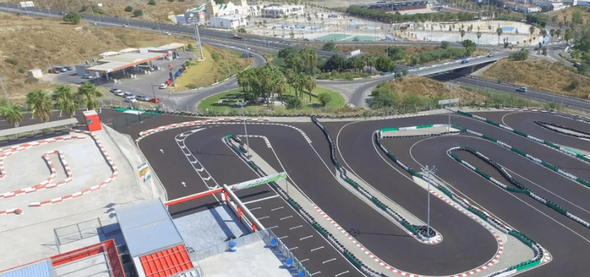 Una vista aérea de Karting en Estepona revela la pista serpenteando elegantemente a través de una exuberante vegetación y carreteras que se cruzan, con un complejo de edificios cercano que realza la pintoresca escena. - ForTwo - Planes para parejas