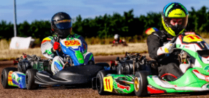 En Karting en Talavera La Real, dos corredores con equipamiento y cascos vibrantes recorren la soleada pista al aire libre, en una competencia reñida. - ForTwo - Planes para parejas