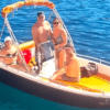 Cuatro personas se relajan en una pequeña embarcación en las cristalinas aguas de Menorca, disfrutando del sol. Sentados o de pie, todos disfrutan de la libertad de estar a bordo de la Lancha Sin Licencia en Menorca bajo un cielo radiante. - ForTwo - Planes para parejas