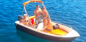 Cuatro personas se relajan en una pequeña embarcación en las cristalinas aguas de Menorca, disfrutando del sol. Sentados o de pie, todos disfrutan de la libertad de estar a bordo de la Lancha Sin Licencia en Menorca bajo un cielo radiante. - ForTwo - Planes para parejas