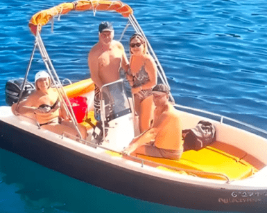 Cuatro personas se relajan en una pequeña embarcación en las cristalinas aguas de Menorca, disfrutando del sol. Sentados o de pie, todos disfrutan de la libertad de estar a bordo de la Lancha Sin Licencia en Menorca bajo un cielo radiante. - ForTwo - Planes para parejas