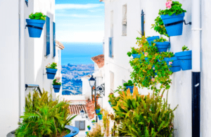 Experimente un día soleado en Mijas, donde estrechos callejones blancos con macetas de flores azules y exuberante vegetación conducen a vistas al mar, como aparece en "Marbella y Mijas: disfruta la Costa del Sol". - ForTwo - Planes para parejas