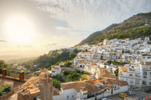 Mientras el atardecer proyecta una cálida luz sobre Mijas, sus edificios blancos se funden con la exuberante vegetación bajo un cielo parcialmente nublado, capturando el encanto de la Costa del Sol. Descubre todo esto en "Marbella y Mijas: disfruta la Costa del Sol". - ForTwo - Planes para parejas