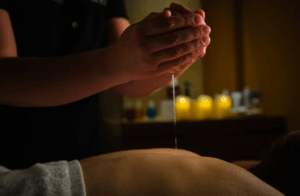 En la sala de masajes a la luz de las velas, la tranquilidad se instala mientras se vierte suavemente aceite sobre la espalda que espera durante el Masaje relax en Balneario Castilla Termal Solares. - ForTwo - Planes para parejas