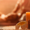 Una vela encendida y aceite de aromaterapia sobre una toalla de spa realzan el ambiente relajante de Castilla Termal Solares. El fondo difuminado ofrece un ambiente sereno, perfecto para disfrutar del lujoso "Masaje relajante en Balneario Castilla Termal Solares". - ForTwo - Planes para parejas