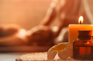Una vela encendida y aceite de aromaterapia sobre una toalla de spa realzan el ambiente relajante de Castilla Termal Solares. El fondo difuminado ofrece un ambiente sereno, perfecto para disfrutar del lujoso "Masaje relajante en Balneario Castilla Termal Solares". - ForTwo - Planes para parejas