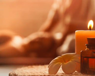 Una vela encendida y aceite de aromaterapia sobre una toalla de spa realzan el ambiente relajante de Castilla Termal Solares. El fondo difuminado ofrece un ambiente sereno, perfecto para disfrutar del lujoso "Masaje relajante en Balneario Castilla Termal Solares". - ForTwo - Planes para parejas