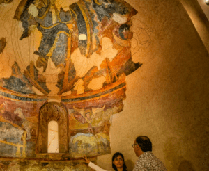 En el Museo de Arte de Girona, suavemente iluminado, dos admiradores se maravillan ante un antiguo mural, cuyos colores vibrantes y figuras cobran vida ante sus ojos. - ForTwo - Planes para parejas