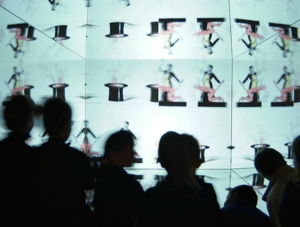 Los visitantes en silueta exploran las pantallas del Museu del Cinema de Girona, donde los sombreros de copa animados y las figuras danzantes cobran vida. - ForTwo - Planes para parejas
