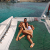 Una pareja se relaja en una red a bordo de la "Navega en Catamarán por Menorca", rodeada por las cristalinas aguas azules cerca de las lejanas costas de Menorca. - ForTwo - Planes para parejas