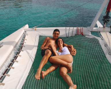 Una pareja se relaja en una red a bordo de la "Navega en Catamarán por Menorca", rodeada por las cristalinas aguas azules cerca de las lejanas costas de Menorca. - ForTwo - Planes para parejas