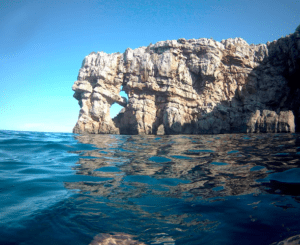 Disfrute de las impresionantes vistas de los acantilados rocosos que se unen a las brillantes aguas azules de Menorca, bajo un cielo despejado. Es el lugar perfecto para disfrutar viendo cómo los catamaranes de Navega en Catamarán por Menorca surcan el horizonte con elegancia. - ForTwo - Planes para parejas