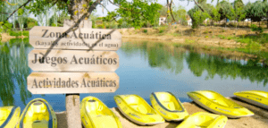 Kayaks amarillos junto al lago y carteles de madera para actividades acuáticas en el Parque de Aventura en Hornachos, rodeado de árboles y jardines. - ForTwo - Planes para parejas