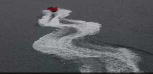 Una vista aérea de un barco rojo en Girona, creando olas blancas en el agua oscura, que recuerdan al Paseo de Acrobacias en el Agua en Girona. - ForTwo - Planes para parejas
