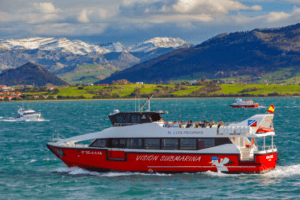 El Paseo en Barco por la Bahía de Santander, una embarcación roja y blanca llamada Visión Submarina, navega por las aguas enmarcadas por montañas nevadas y exuberantes colinas verdes. - ForTwo - Planes para parejas