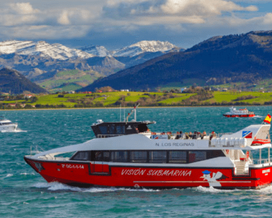 El Paseo en Barco por la Bahía de Santander, una embarcación roja y blanca llamada Visión Submarina, navega por las aguas enmarcadas por montañas nevadas y exuberantes colinas verdes. - ForTwo - Planes para parejas