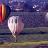 Tres globos vibrantes flotan sobre el paisaje verde y amarillo de Almodóvar del Río, con árboles y edificios distantes que crean un telón de fondo sereno para este encantador Paseo en Globo por Almodóvar del Río. - ForTwo - Planes para parejas