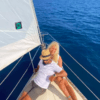Una pareja se relaja en la cubierta de un velero bajo el cielo azul y el mar en calma de la Costa Brava, disfrutando de su tranquilo Paseo exclusivo en Velero en la Costa Brava. - ForTwo - Planes para parejas