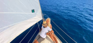 Una pareja se relaja en la cubierta de un velero bajo el cielo azul y el mar en calma de la Costa Brava, disfrutando de su tranquilo Paseo exclusivo en Velero en la Costa Brava. - ForTwo - Planes para parejas